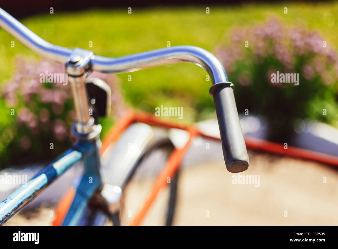 Vintage bicycle handlebar detail close up with parking bokeh background in flower bed in sunny day Stock Photo