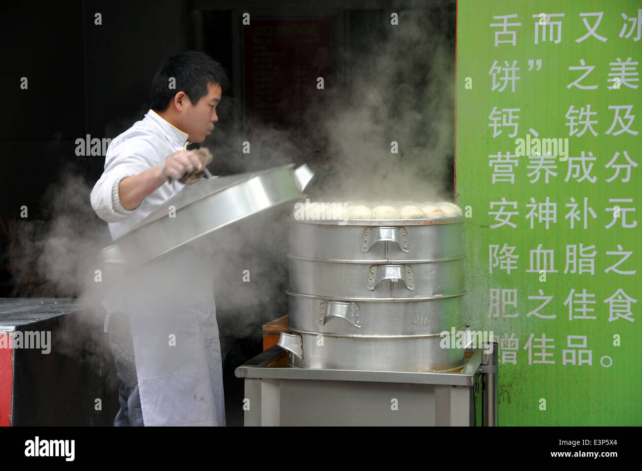 PENGZHOU, CHINA: Cook lifts the cover off a stack of freshly steamed bao zi buns Stock Photo
