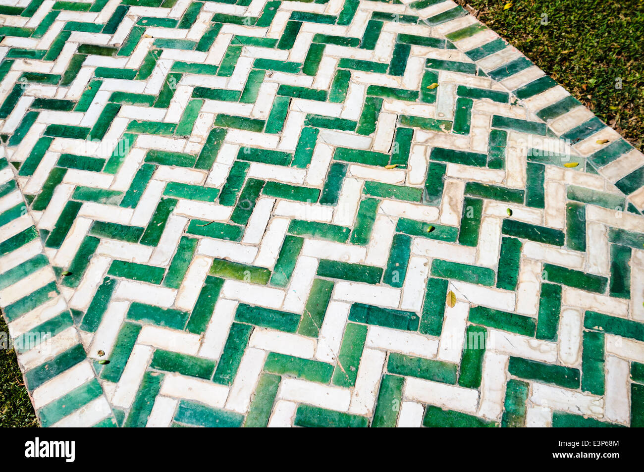 Garden path made from green and white rectangular ceramic tiles, laid in a herringbone pattern. Stock Photo