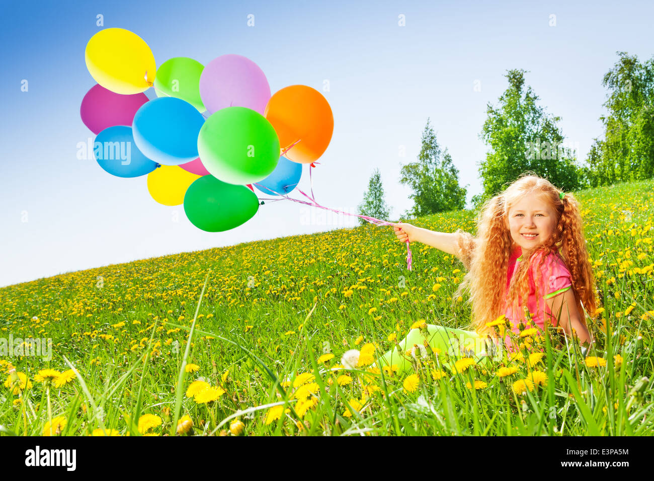 Cheerful girl with flying balloons sits on grass Stock Photo Alamy