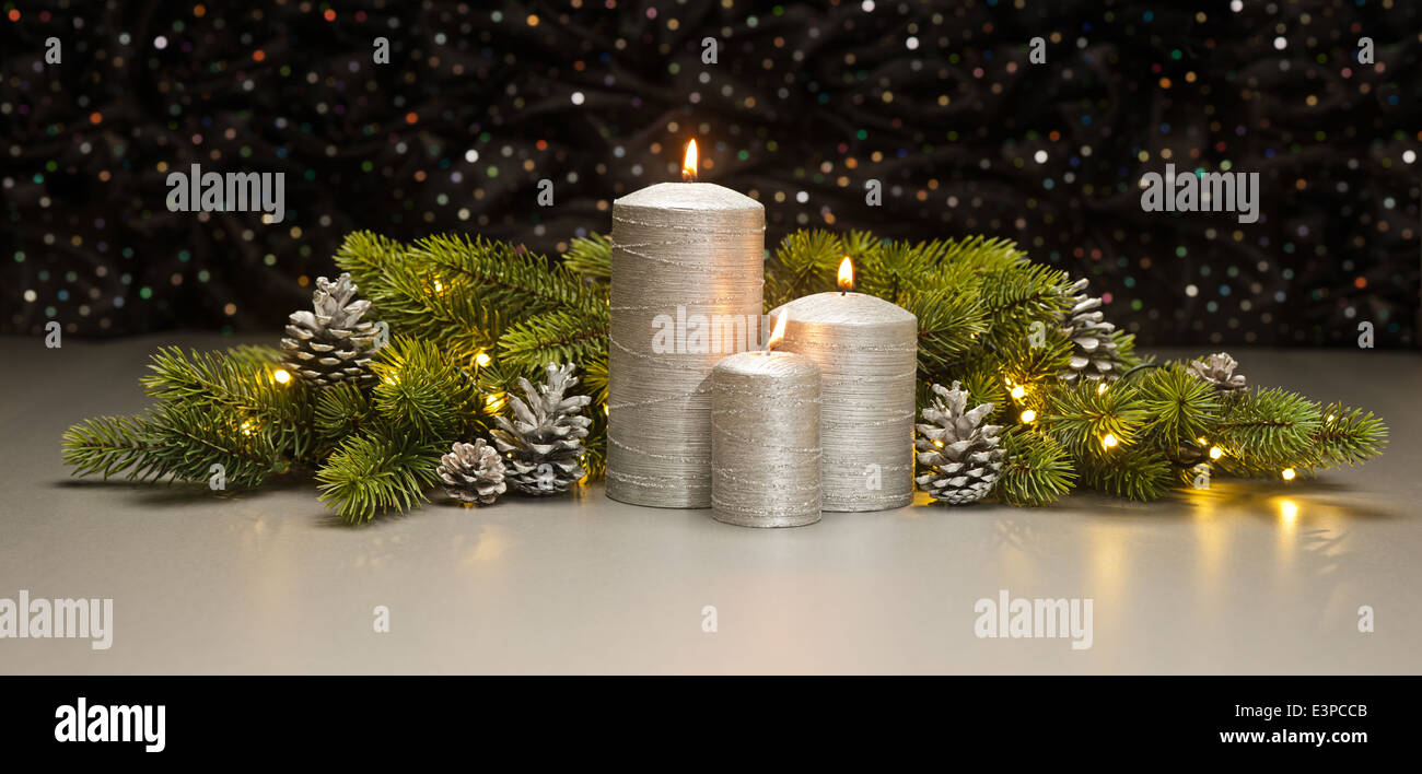 Three Silver Candles with Christmas tree branches and pine cones decorated Stock Photo