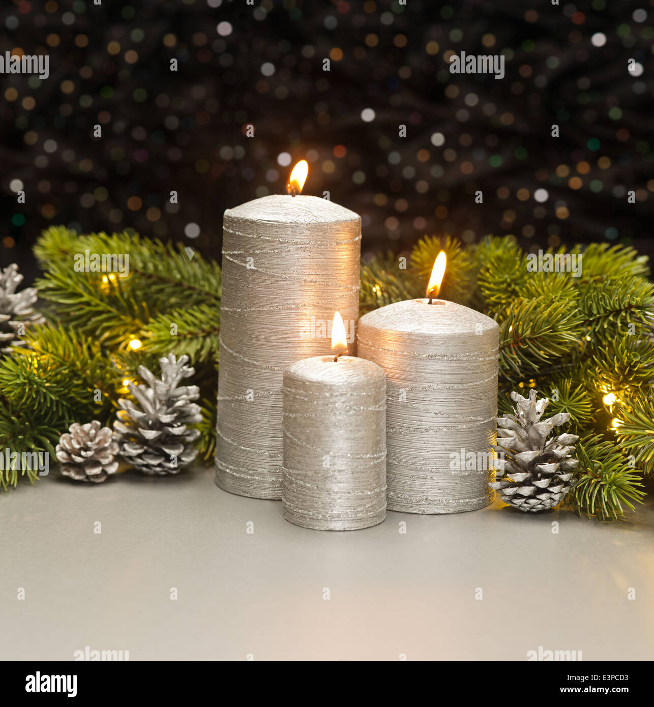 Three Silver Candles with Christmas tree branches and pine cones decorated Stock Photo
