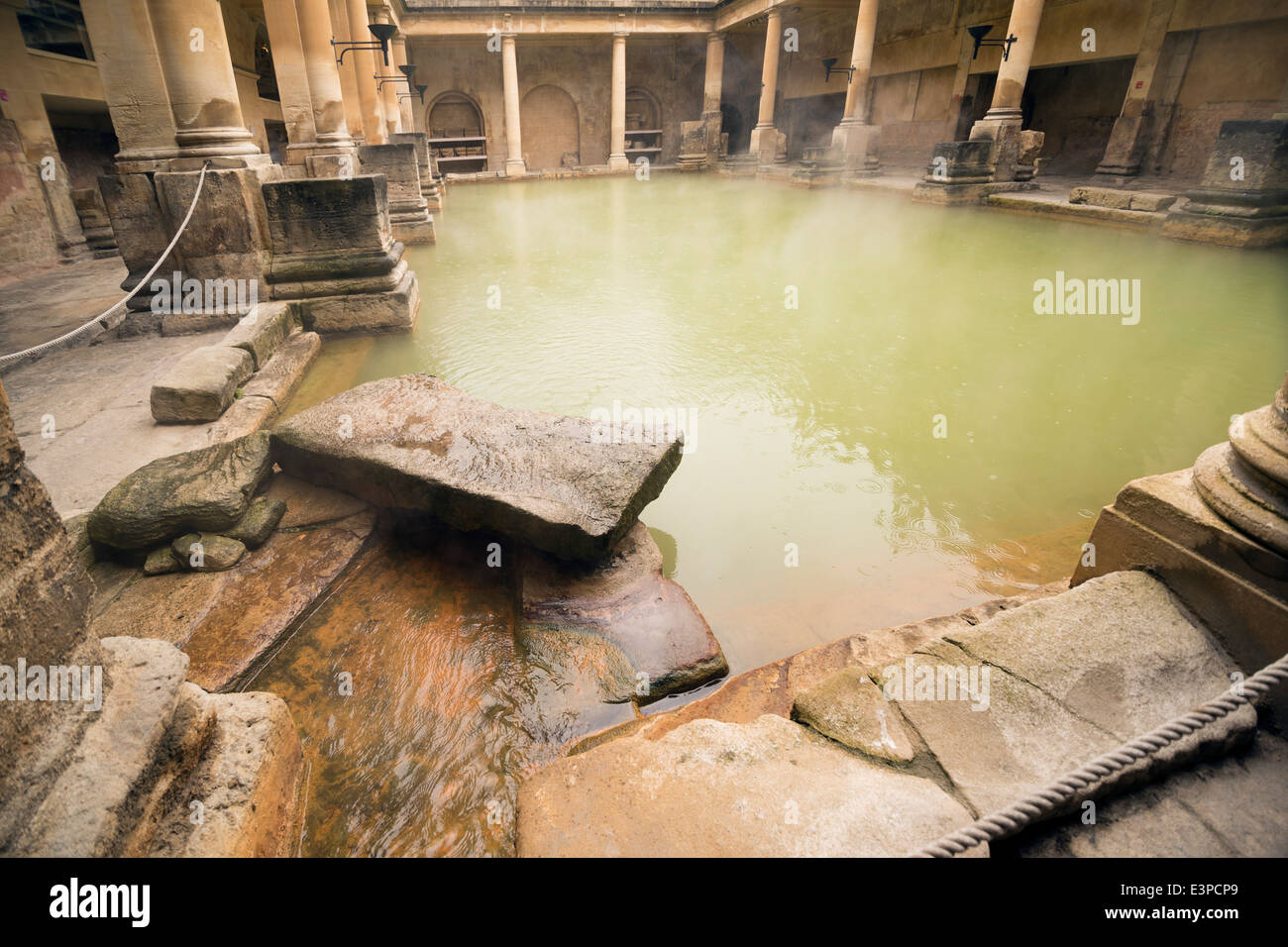 Stone and columns around the steamy water at the Roman Bath in Bath