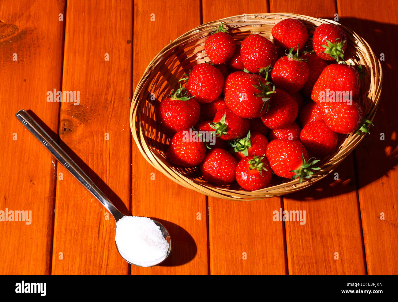 Strawberries in a basket with a spoonful of sugar on a wooden ...