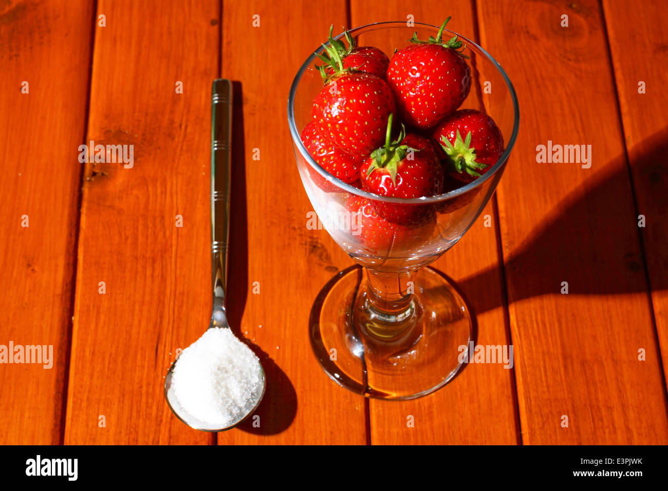 Strawberries in a glass with a spoonful of sugar on a wooden background ...