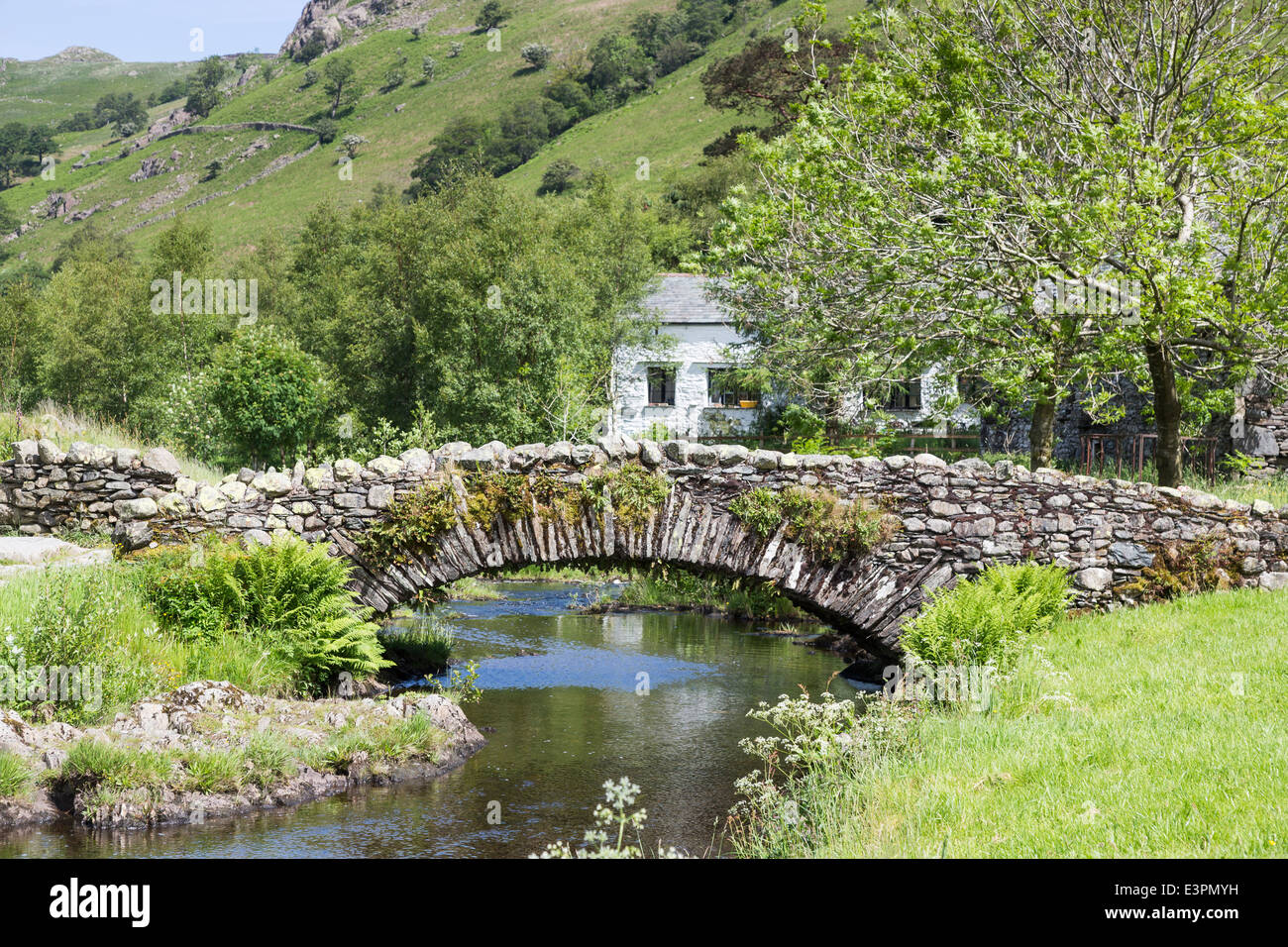 Traditional drystone built Packhorse Bridge at Watendlath, Borrowdale, Lake District with pretty whitewashed stone cottage Stock Photo