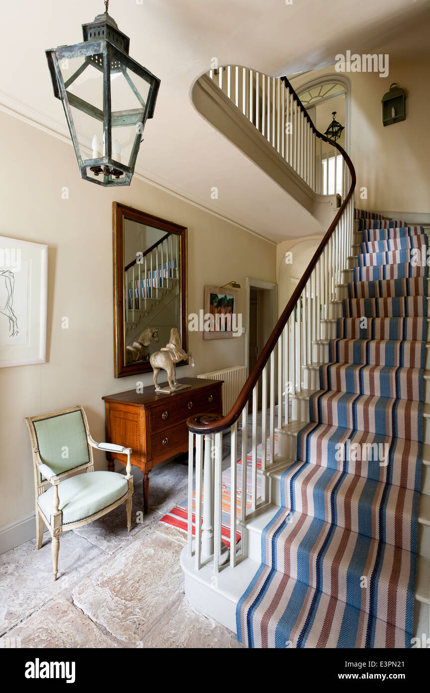 Striped Christine van der Hurd runner on staircase with wooden banister in flagstone entrance hall with antique armchair Stock Photo