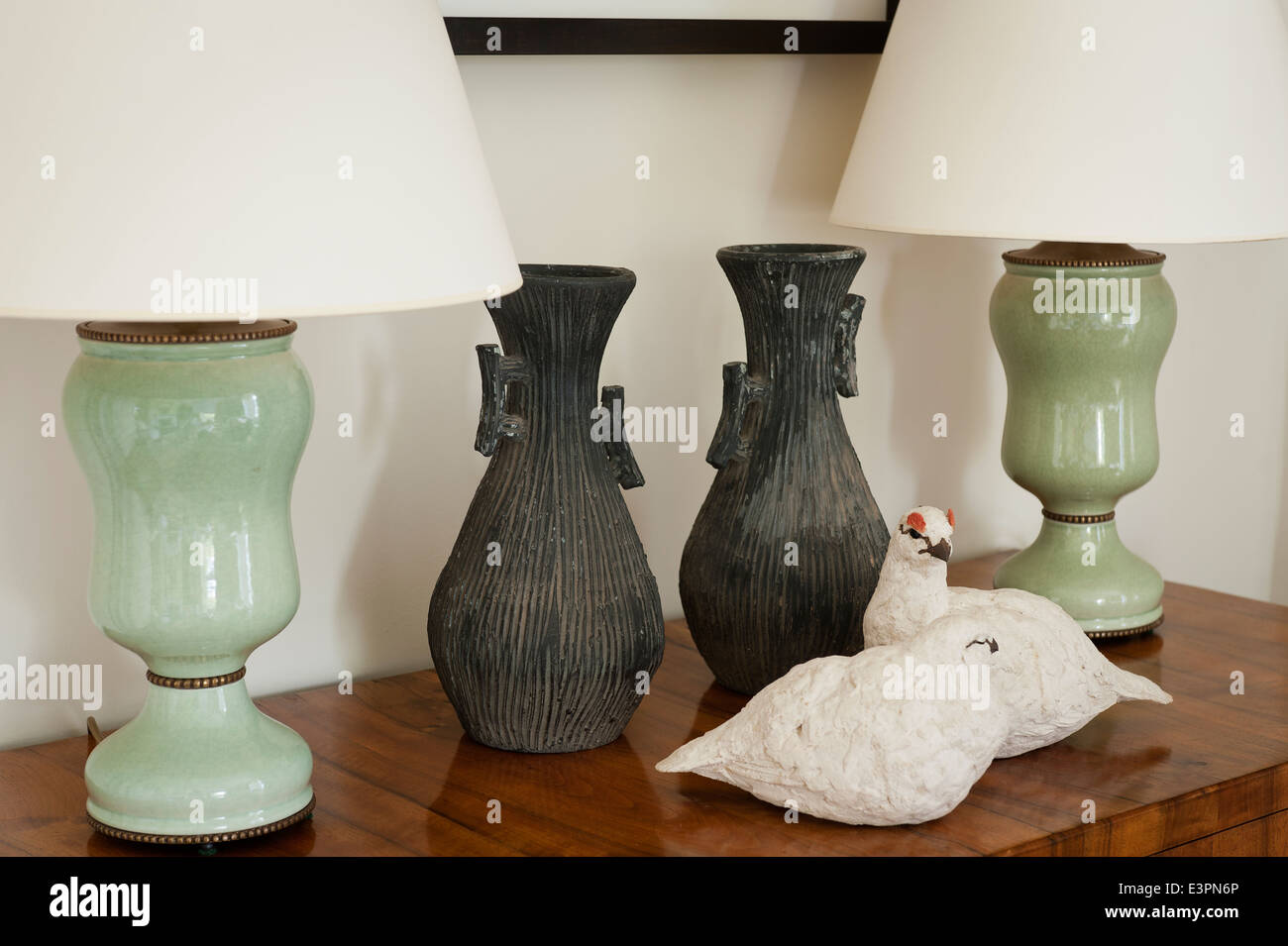 A pair of green lamps on wooden chest top with pair of rustic made vases and bird sculptures Stock Photo