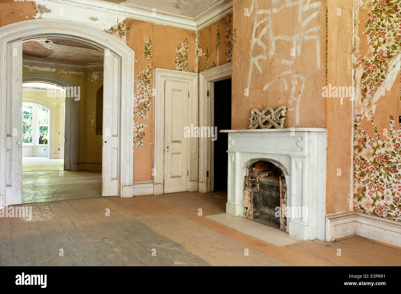 Old bricked up fireplace in empty room with peeling wallpaper and unsanded floors Stock Photo