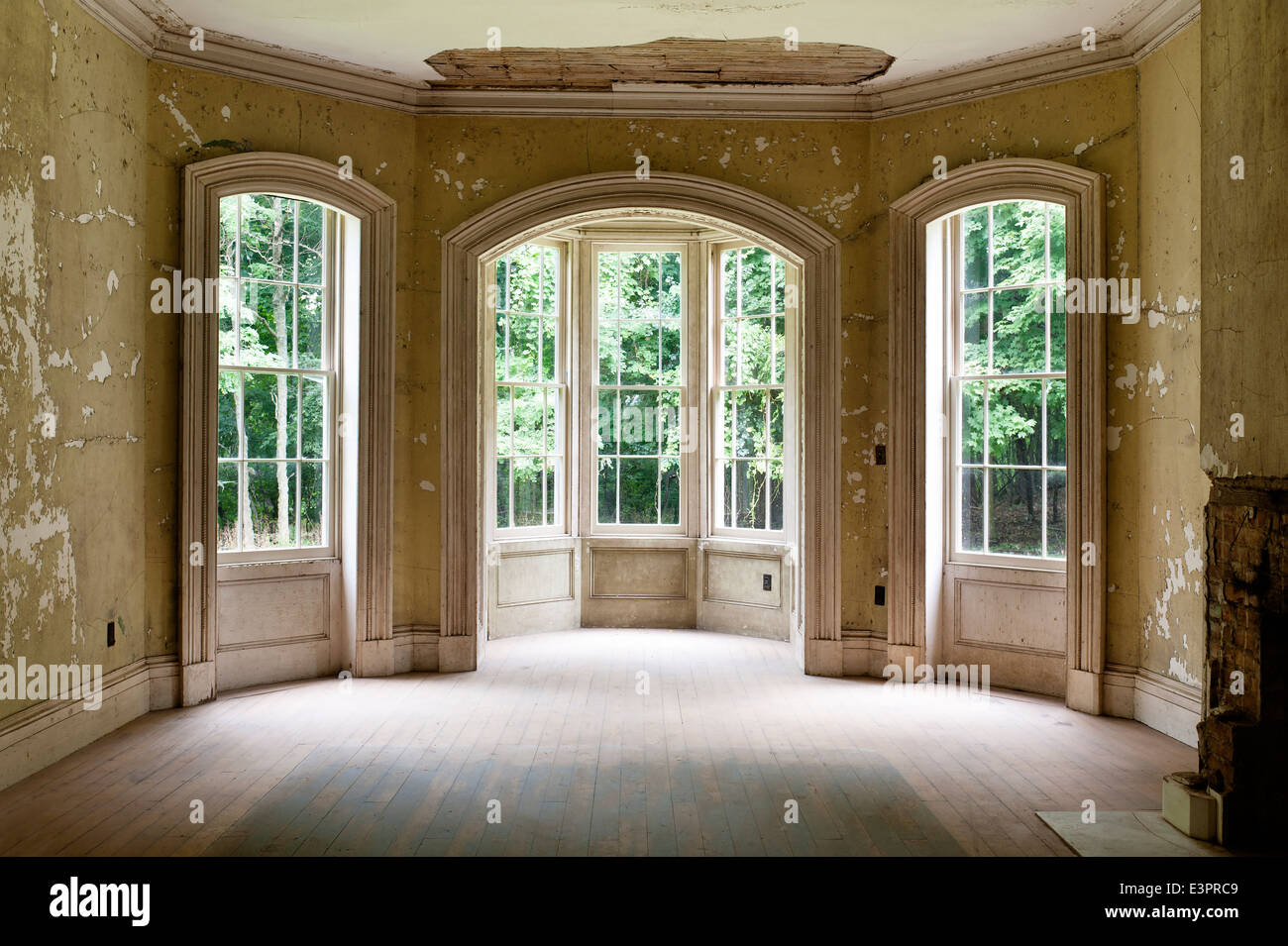 Tripartite window in empty room with peeling wallpaper and damaged ceiling Stock Photo