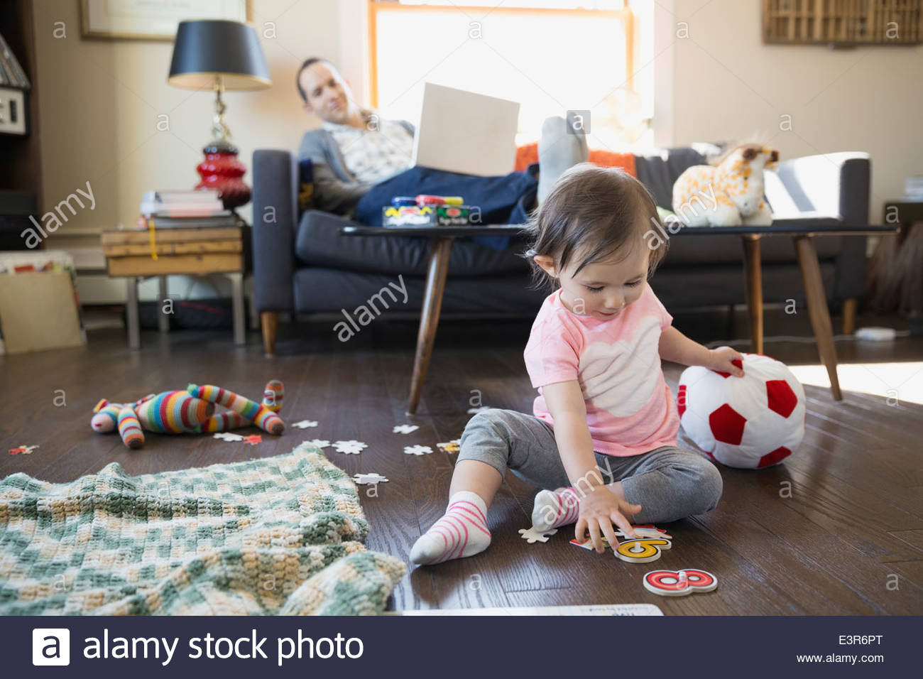 Father with laptop watching baby daughter play Stock Photo