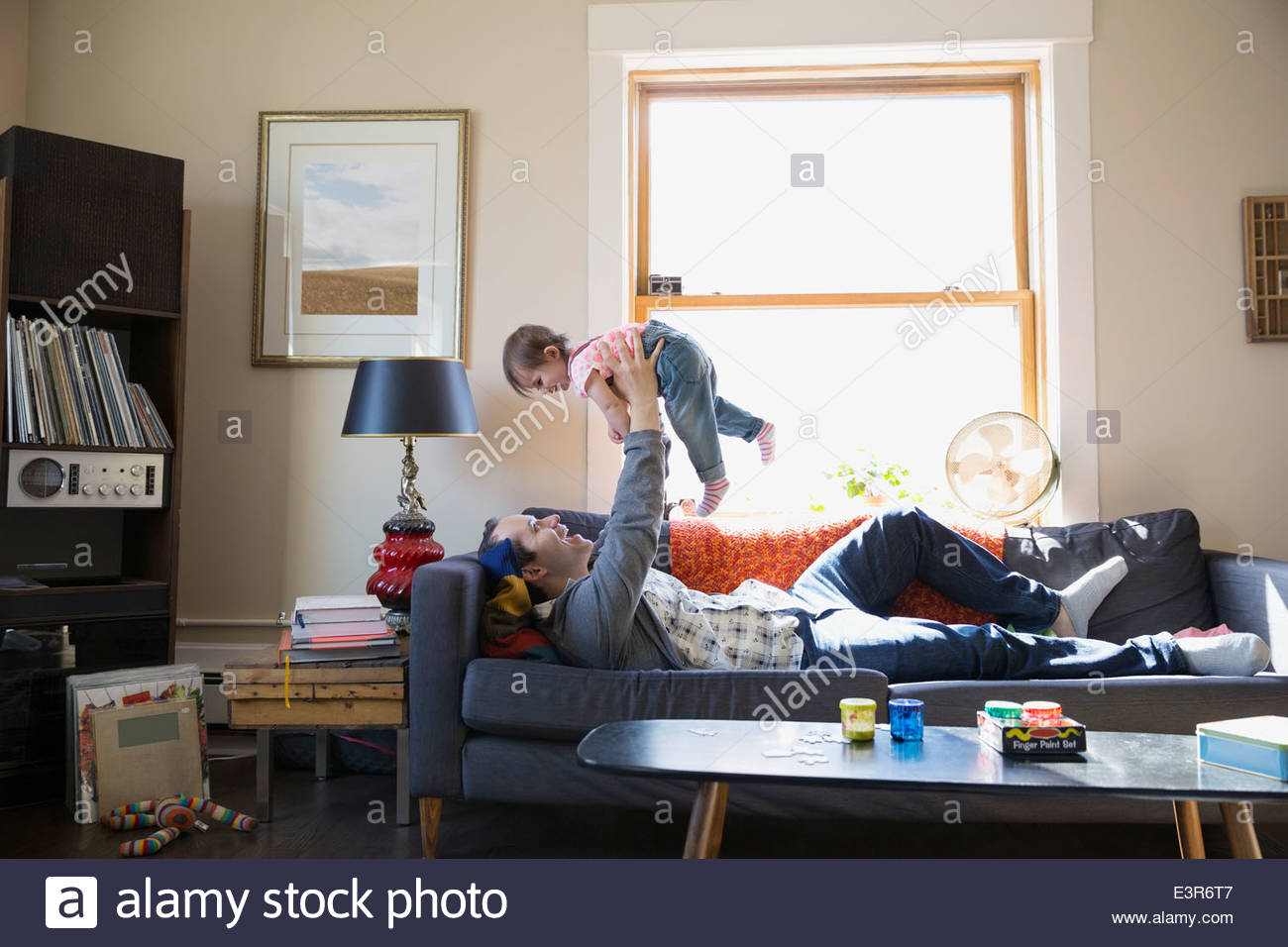 Father lifting baby daughter overhead on sofa Stock Photo