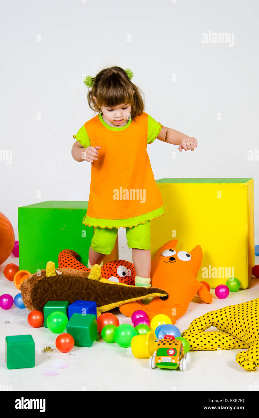 Little caucasian girl is standing among toys Stock Photo - Alamy