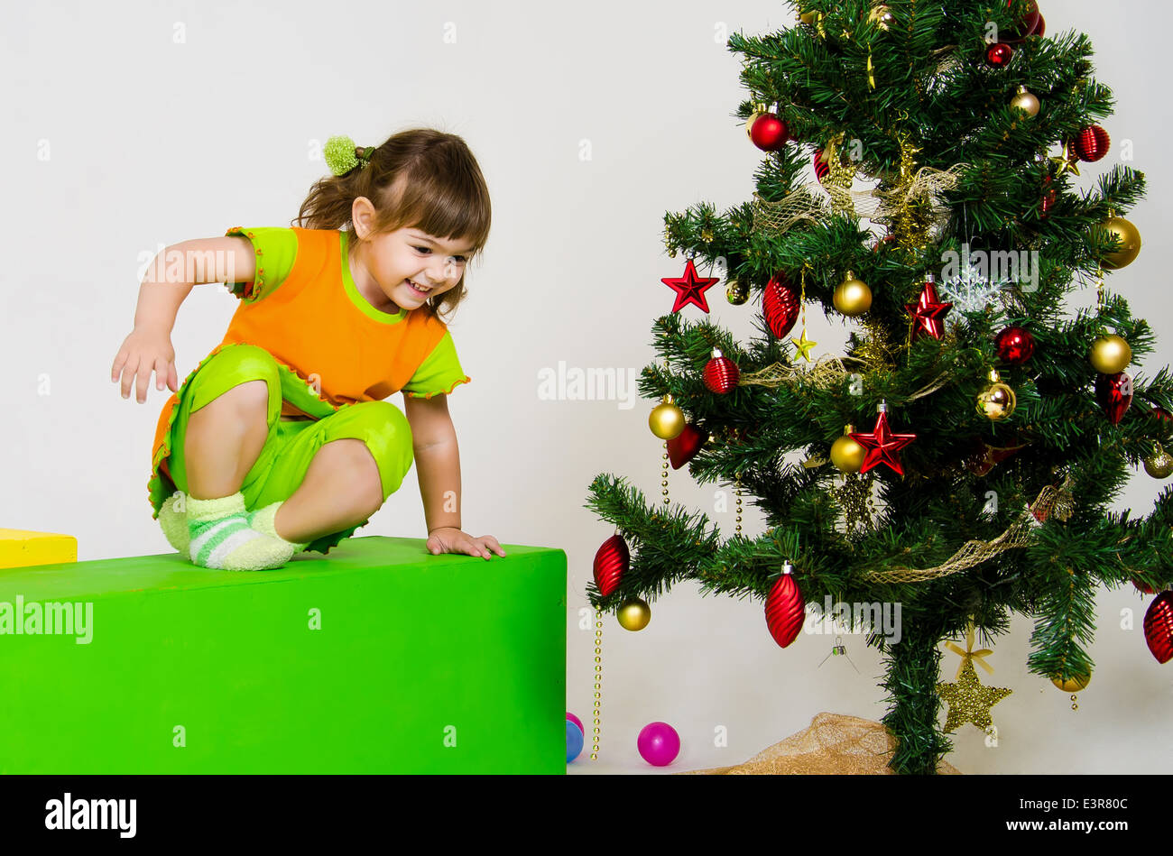 Cute little caucasian girl is playing near christmas tree indoors Stock Photo