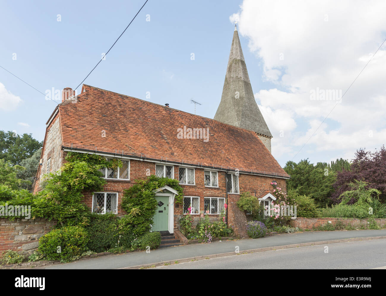 Fourteenth century cottage and St Peter's church spire in Ash, Guildford, Surrey with hollyhocks, roses around the windows Stock Photo