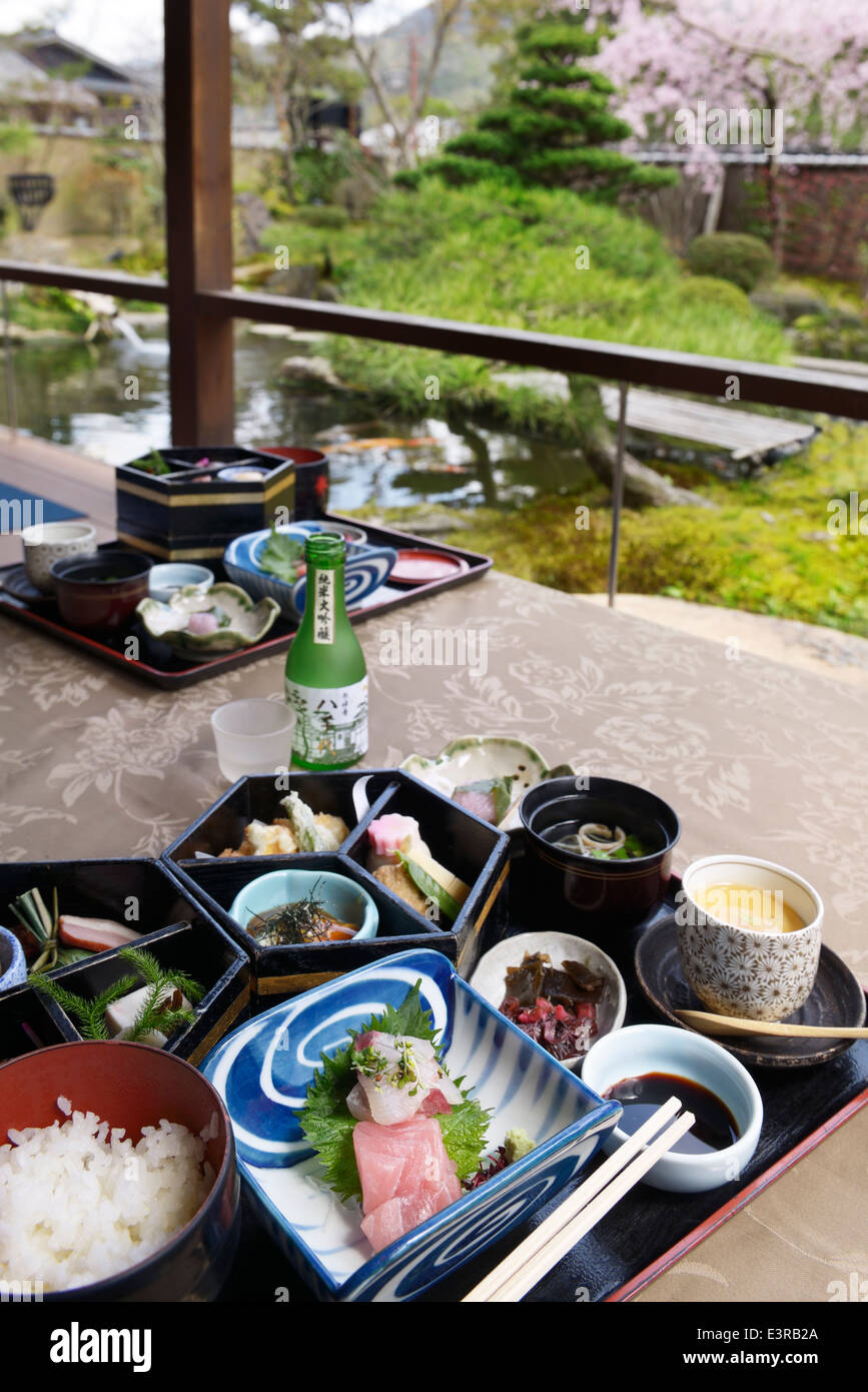 Japanese breakfast meal and sake on a patio of a ryokan hotel with garden in the background. Kyoto, Japan. Stock Photo