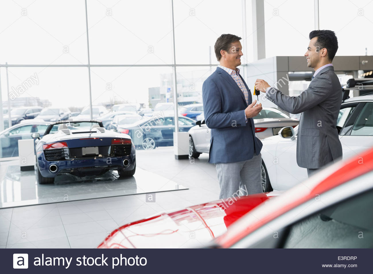 Salesman giving man keys in car dealership showroom Stock Photo