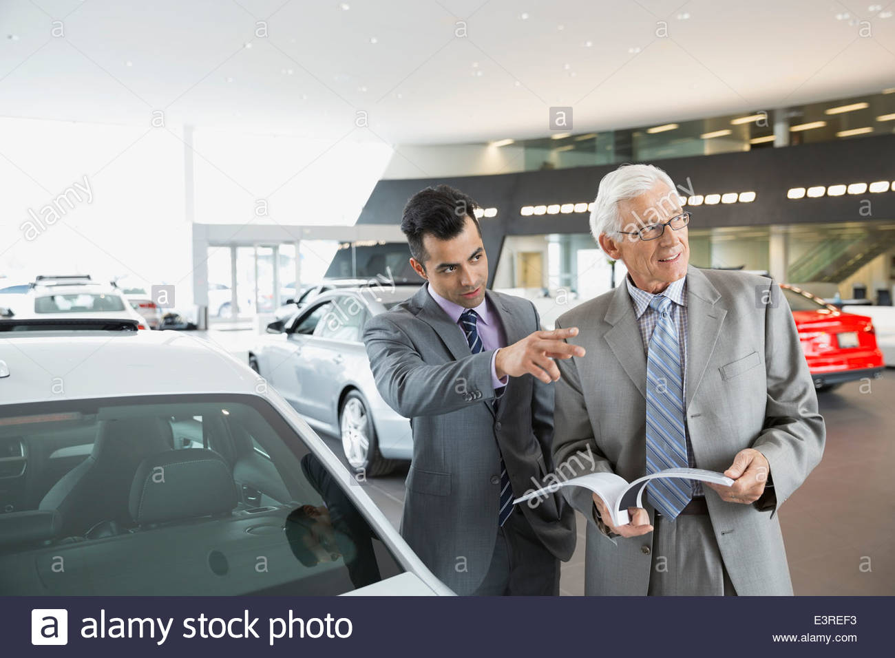 Salesman pointing in car dealership showroom Stock Photo Alamy