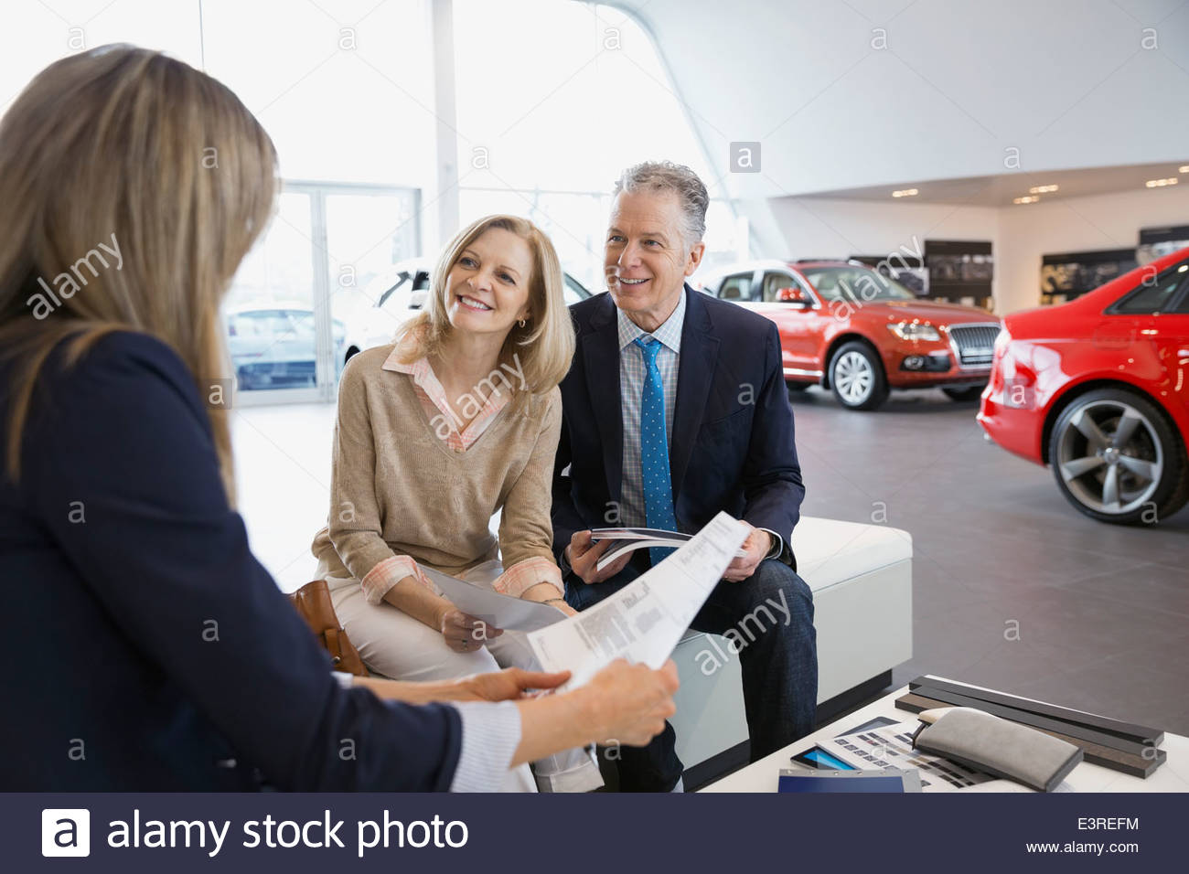 Saleswoman and couple finalizing paperwork in car dealership Stock
