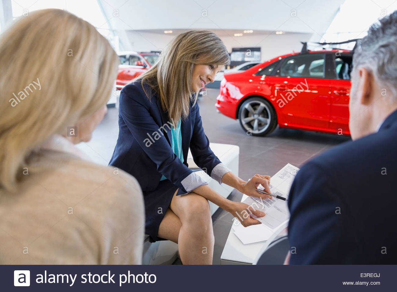 Saleswoman and couple finalizing paperwork in car dealership Stock