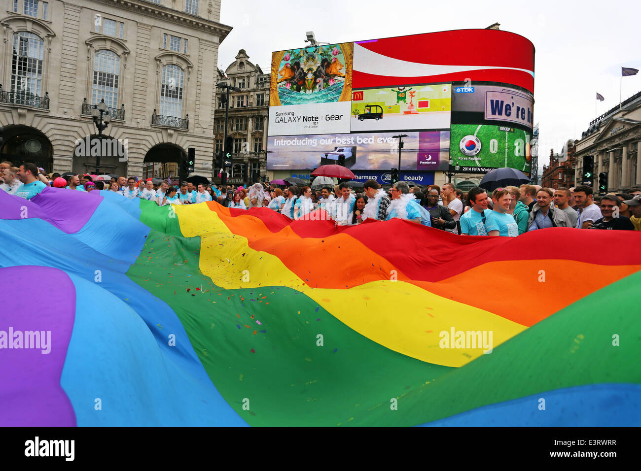 London, UK. 28th June 2014. Giant rainbow flag at Piccadilly Circus at the Pride London Parade 2014 in London. Rain storms throughout the day didn't dampen the spirits of the 20,000 people in the parade of the crowds in the packed streets watching. It did however bring out plenty of rainbow umbrellas. Credit:  Paul Brown/Alamy Live News Stock Photo