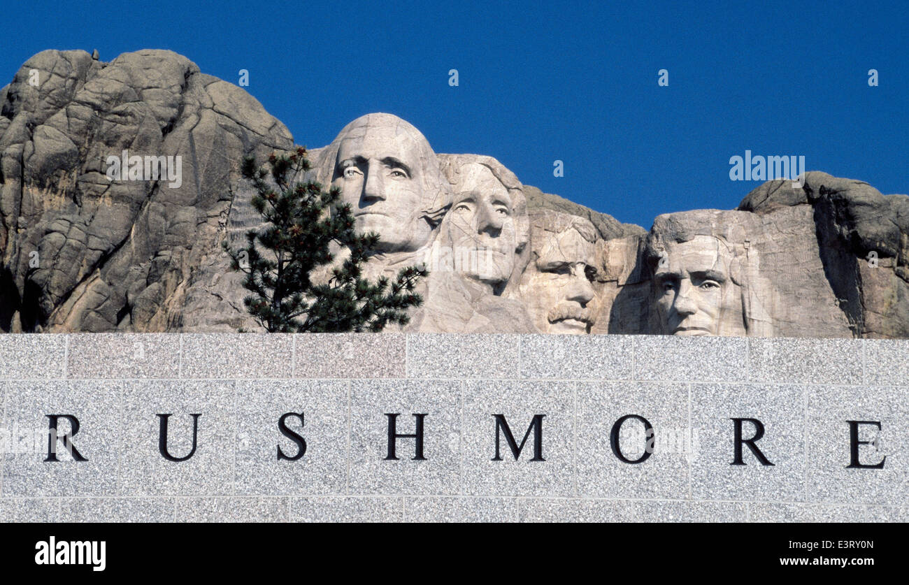 The faces of four U.S. Presidents carved on a mountain look over a Mount Rushmore National Memorial sign in the Black Hills of South Dakota, USA. Stock Photo