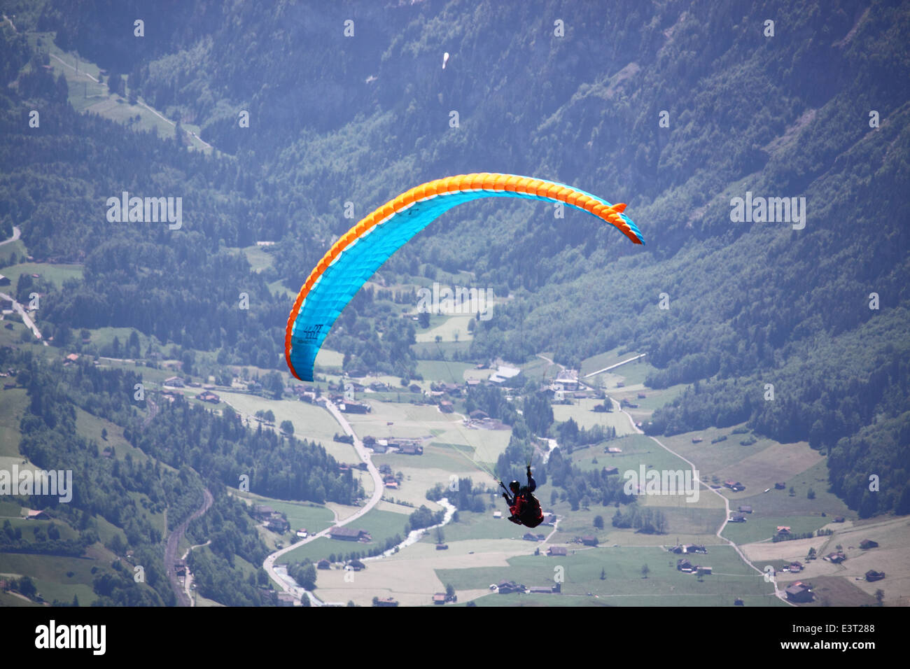 A blue paraglider with forests and fields in the background. Stock Photo