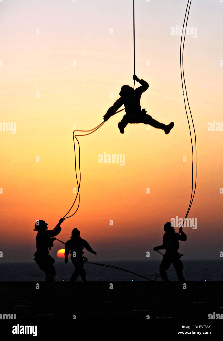 US Marines with Battalion Landing Team, 22nd Marine Expeditionary Unit, rappel out of a CH-53E Super Stallion helicopter at sunset during a fast rope and rappel training exercise aboard the USS Bataan June 24, 2014. Stock Photo