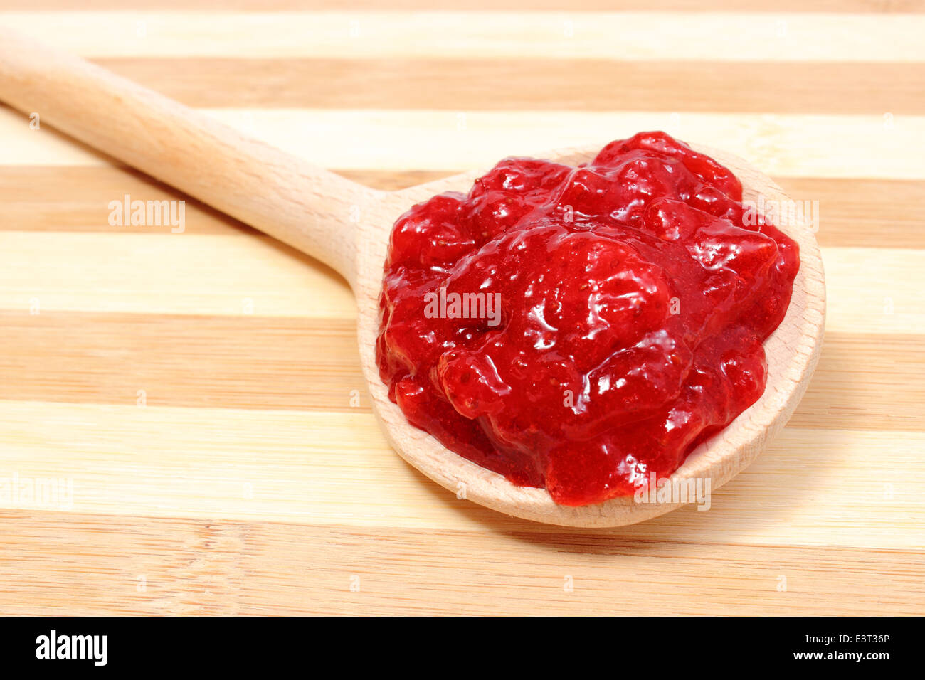 Homemade strawberry jam on wooden spoon lying on wooden cutting board Stock Photo