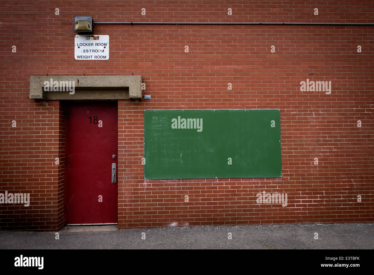 A red locker room door on a brick wall next to a green chalkboard Stock Photo