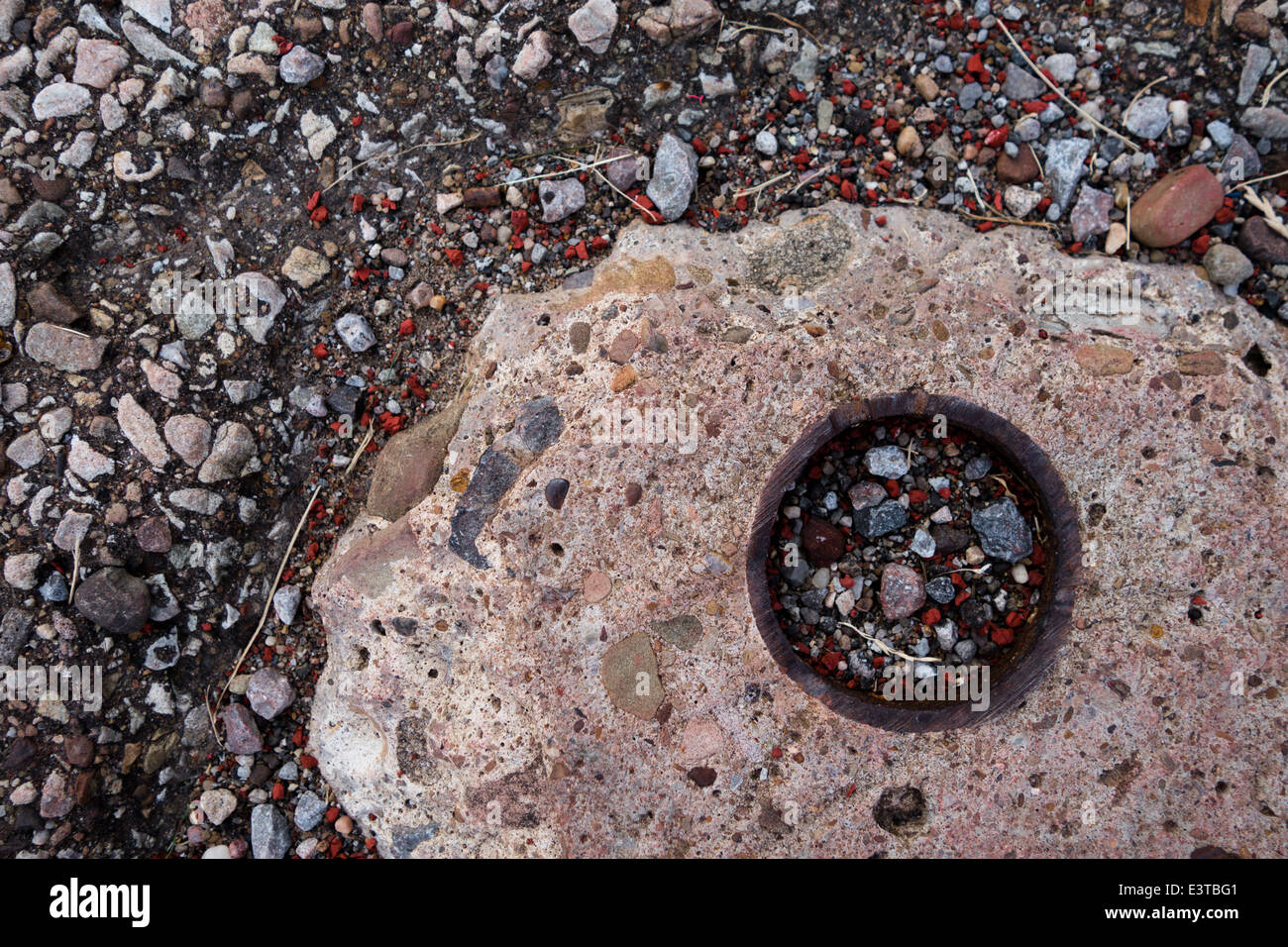 A circular hole on a sidewalk is filled with gravel and pebbles Stock