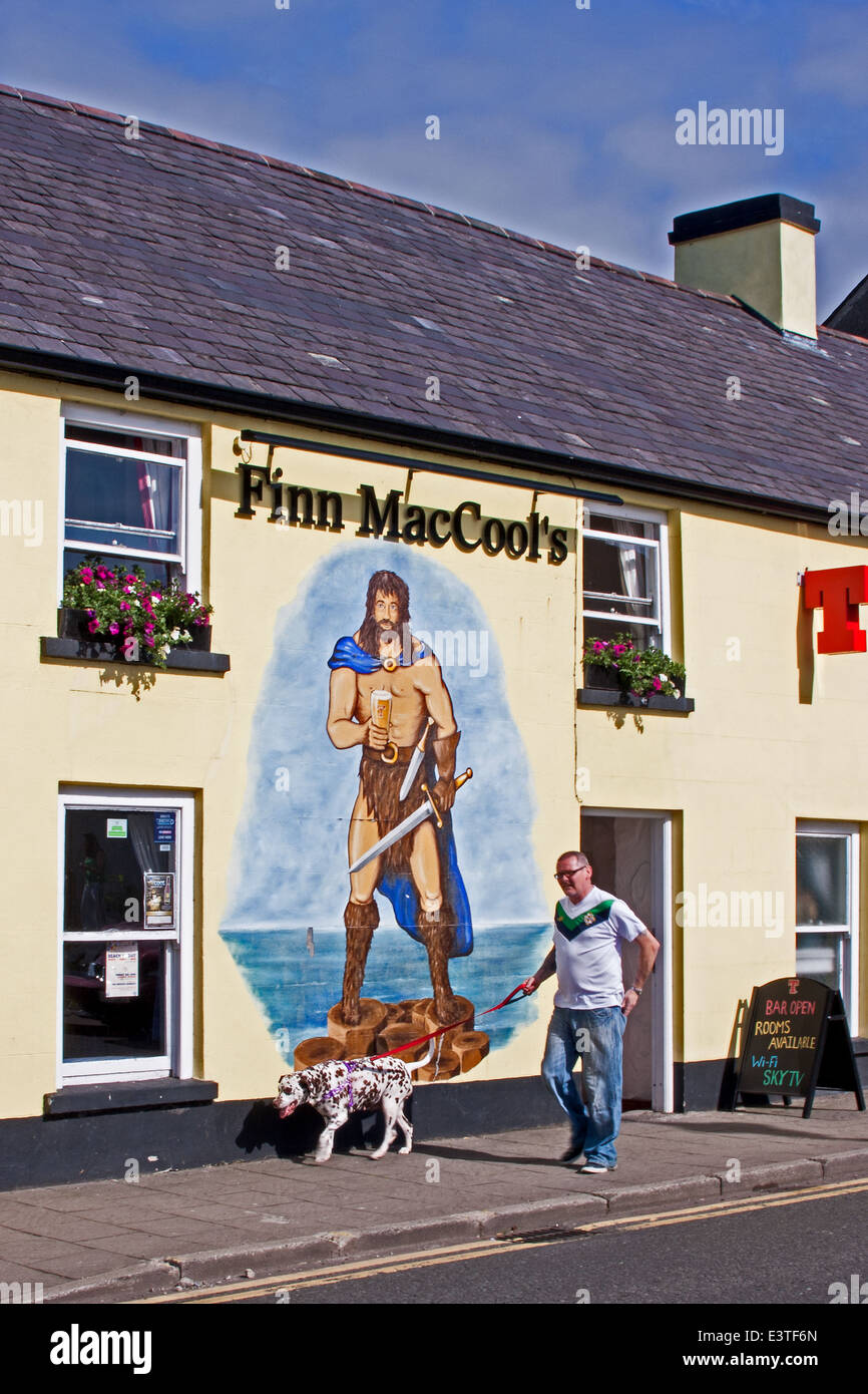 Man and dog walk past mural of Finn MacCool on Finn MacCool's pub in Bushmills, Co. Antrim,  Ulster, Northern Ireland Stock Photo
