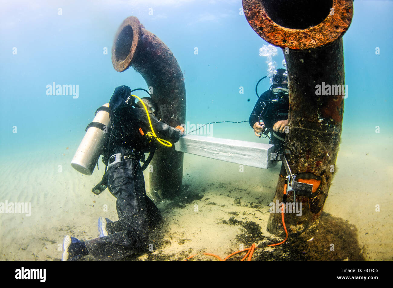 Commercial divers attach a zinc anode to a brine discharge pipe Stock Photo