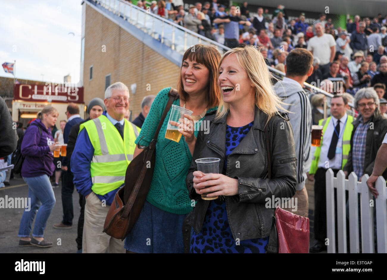 Young women 20s laughing and drinking at a floodlit cricket match Hove Sussex UK Stock Photo