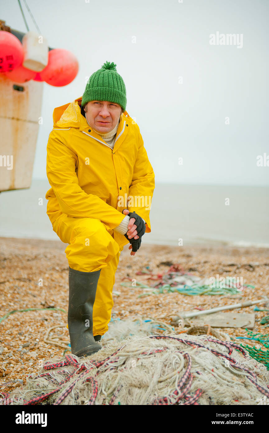 Sea fisherman, wearing bright yellow water proof overalls, standing over a  pile of fishing nets Stock Photo - Alamy