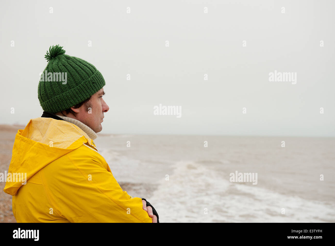 Sea fisherman wearing bright yellow water proof overalls, keeping a watchful eye across the sea. Stock Photo