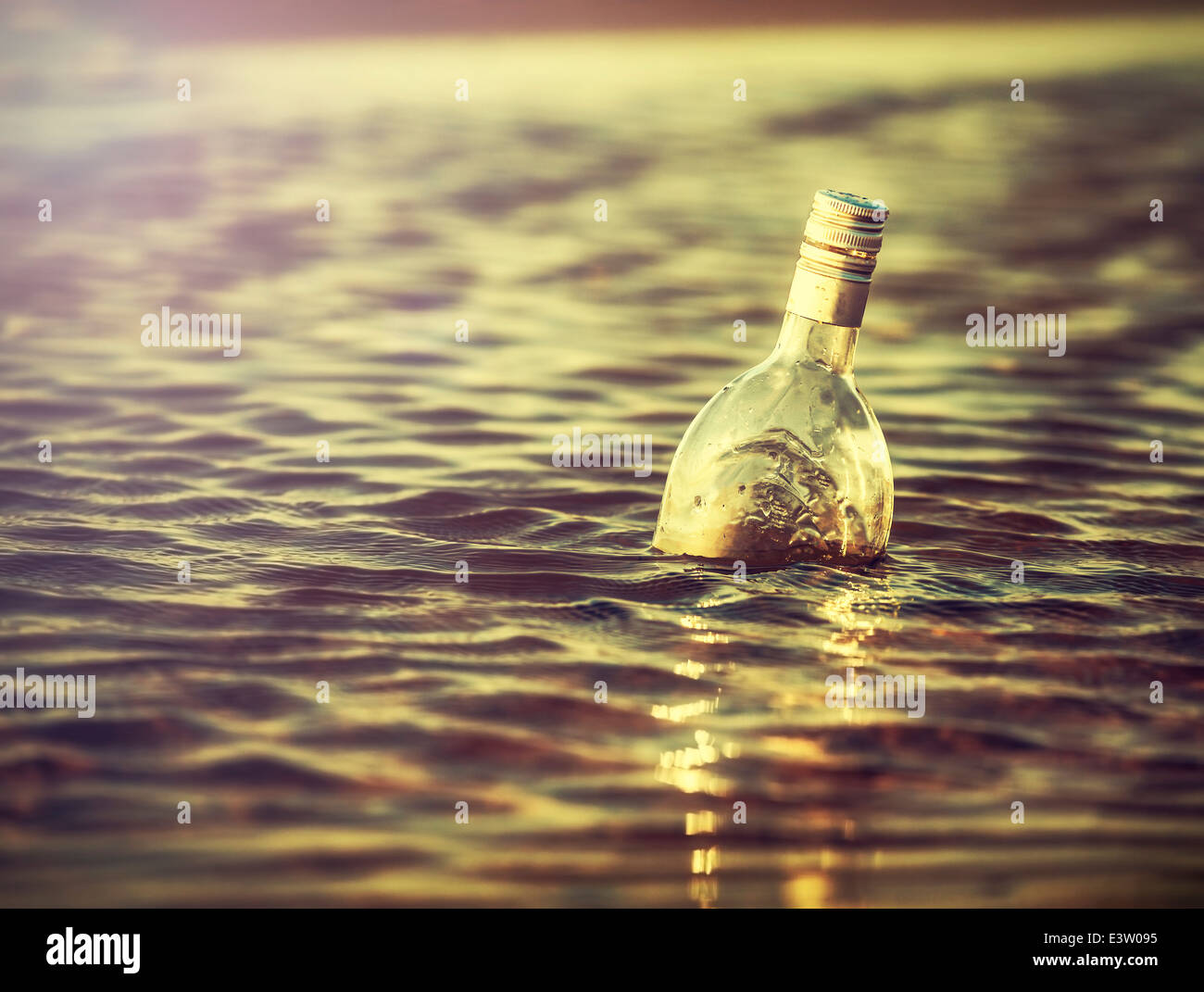 Bottle in water at sunset, retro instagram vintage effect. Stock Photo