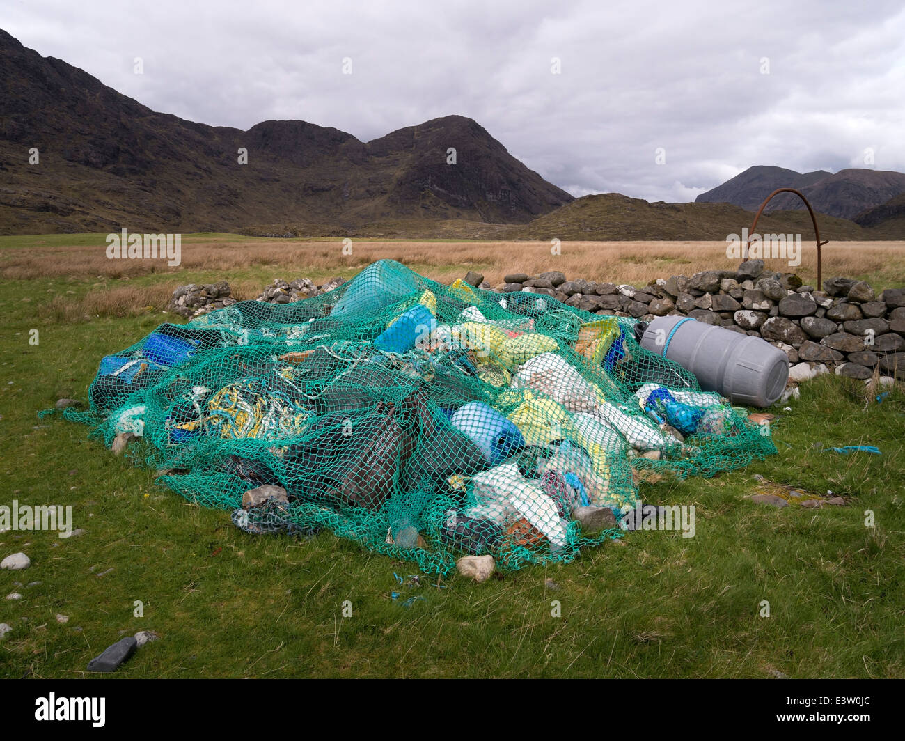 Collection of beach rubbish (flotsam and jetsam) under old fishing net at Camasunary Bay, Isle of Skye, Scotland, UK Stock Photo