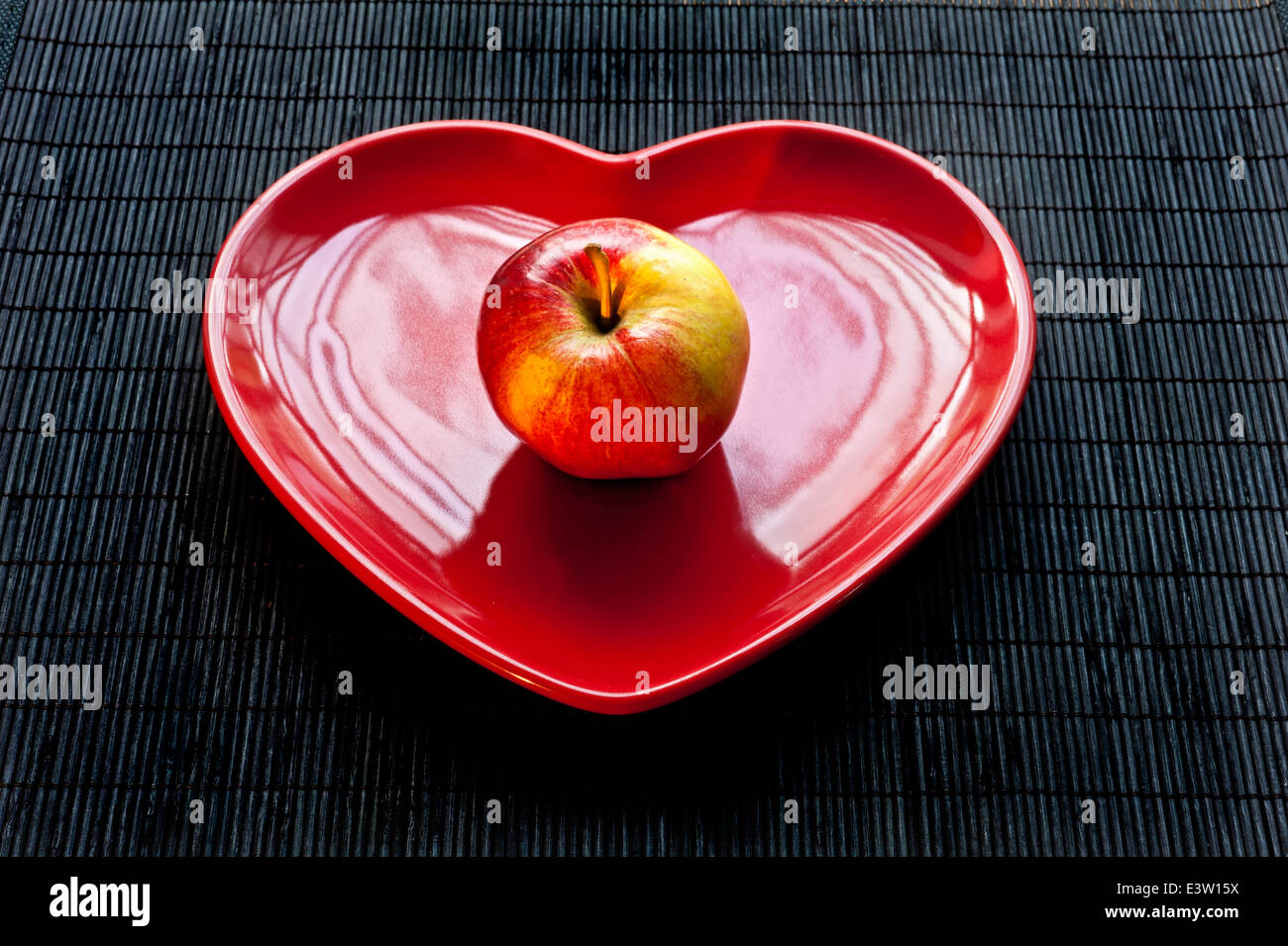 Gala apple on red heart shaped plate, healthy fresh eating regime. Stock Photo