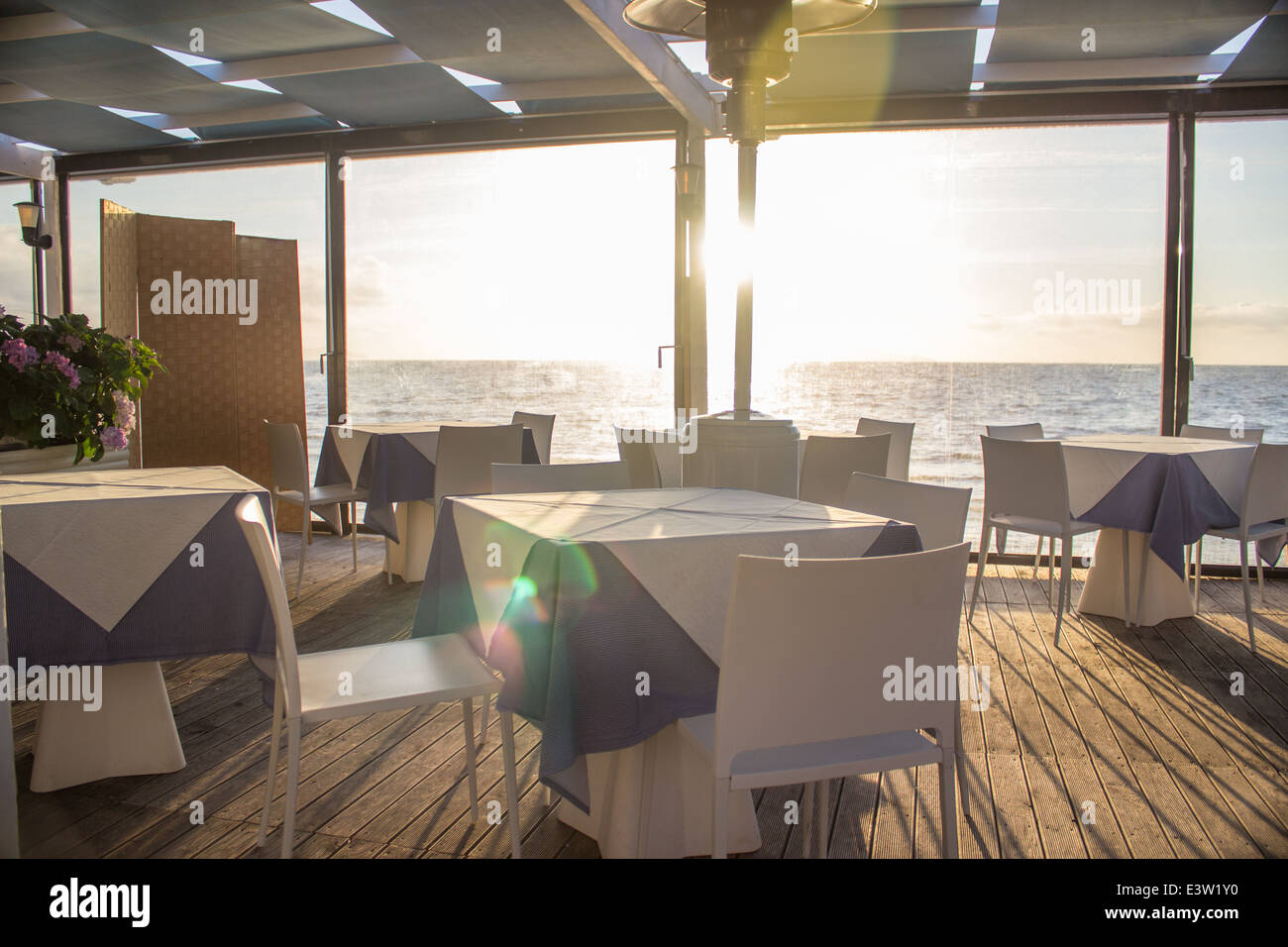 'set table'cafe restaurant sunset 'lens flare' sea horizon [beach cafe] [sea restaurant] 'wooden floor' 'through window' Stock Photo