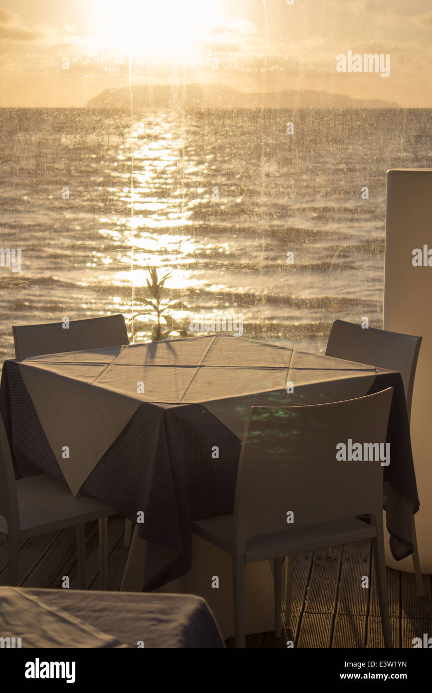 'set table'cafe restaurant sunset 'lens flare' sea horizon [beach cafe] [sea restaurant]  'through window' vertical sun yellow Stock Photo