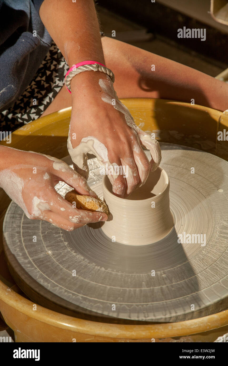 A clay pot is spun on a potter's wheel in a high school pottery class in San Clemente, CA. Note sponge to shape the moist clay. Stock Photo