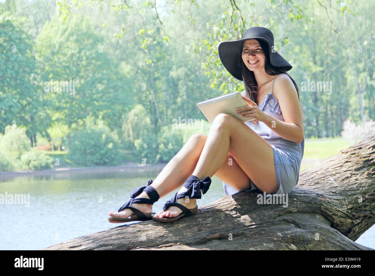 Young woman using tablet outdoor sitting on tree near lake Stock Photo