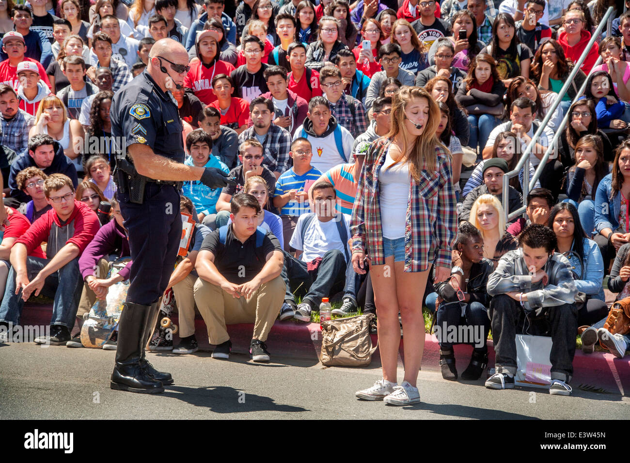 A volunteer high school girl plays the part of a driver being interrogated by a policeman in a dramatization of the danger of drunk driving in Anaheim, CA. Note multiracial student audience in background. Stock Photo