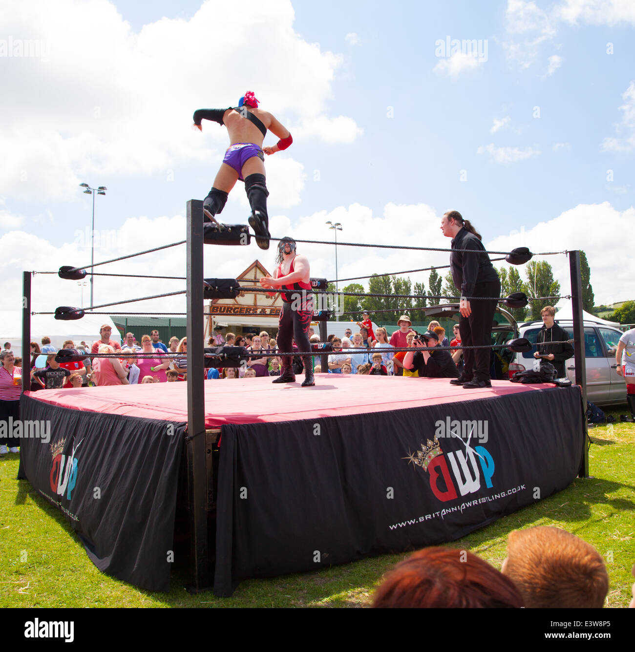 A wrestler wearing a mask leaping off the ropes onto his opponent watched by a crowd at Denbigh town summer carnival Stock Photo
