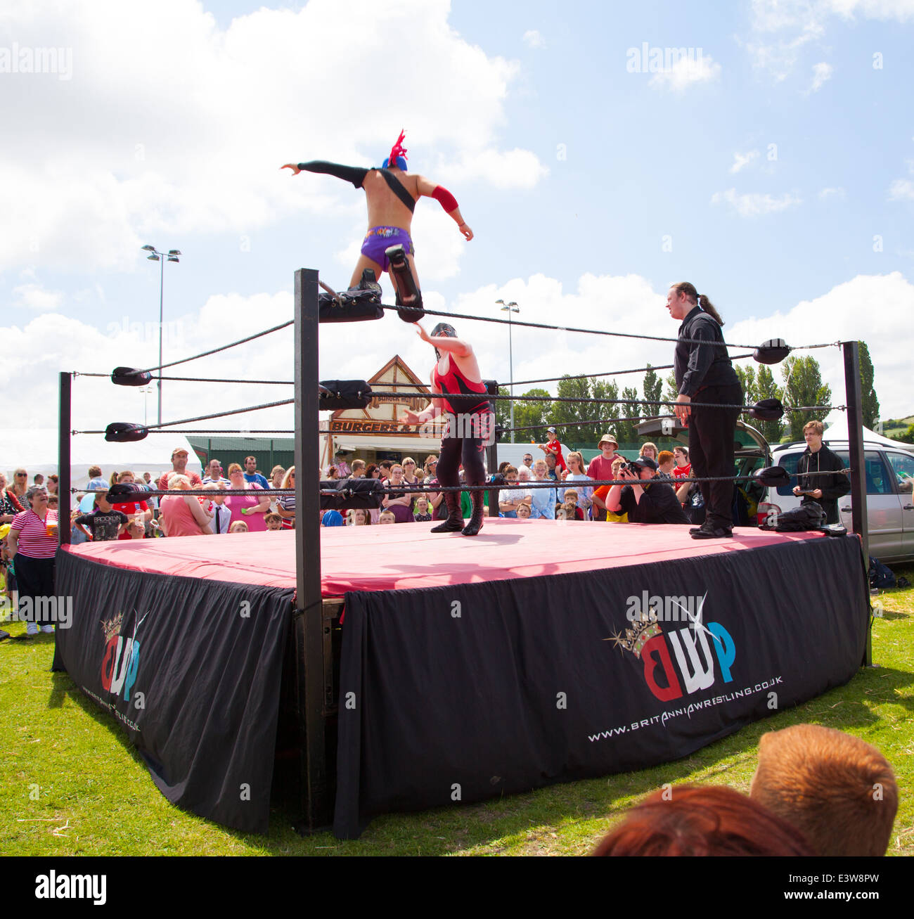 A wrestler wearing a mask leaping off the ropes onto his opponent watched by a crowd at Denbigh town summer carnival Stock Photo