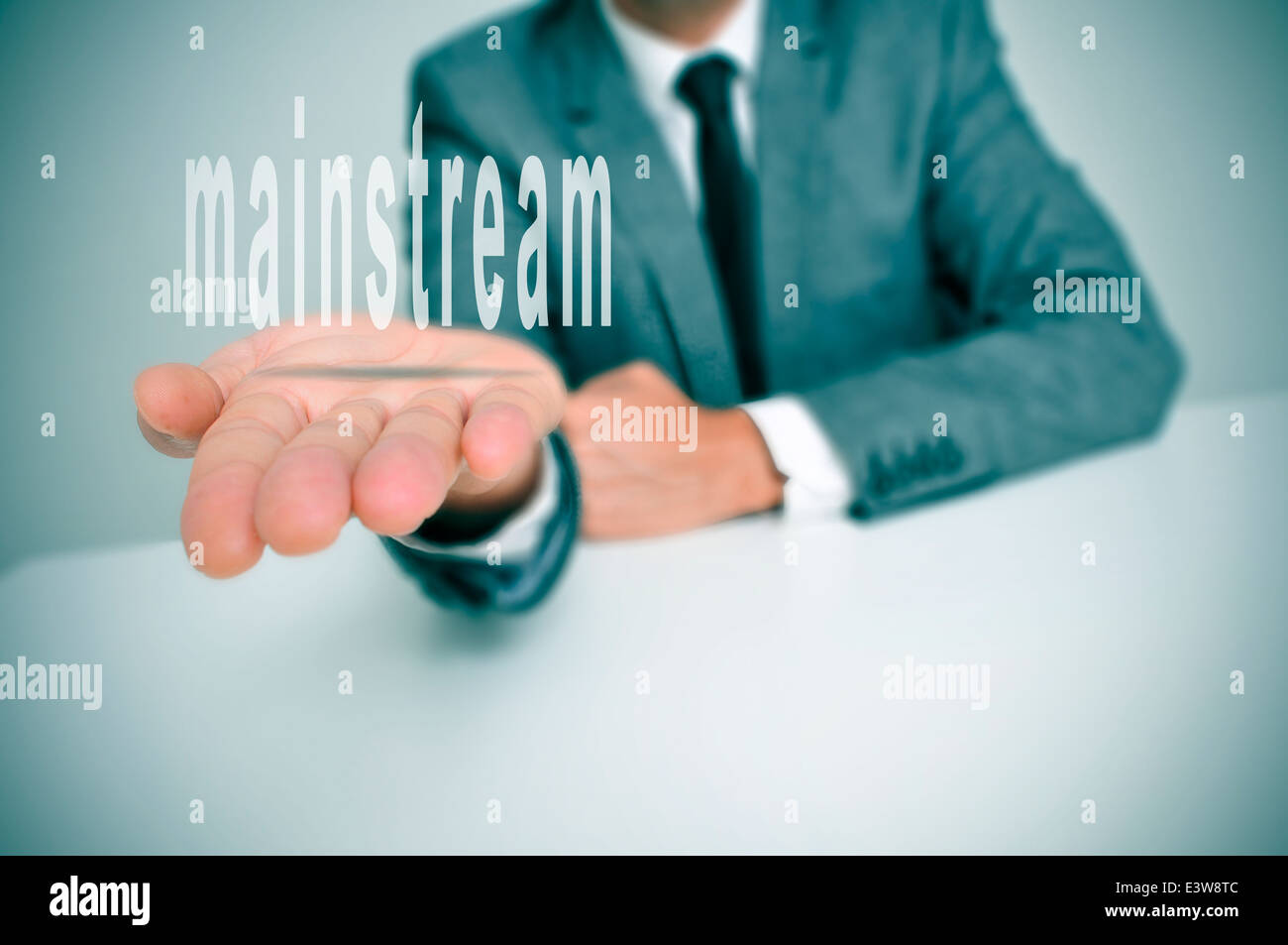man wearing a suit sitting in a desk holding the word mainstream in his hands Stock Photo