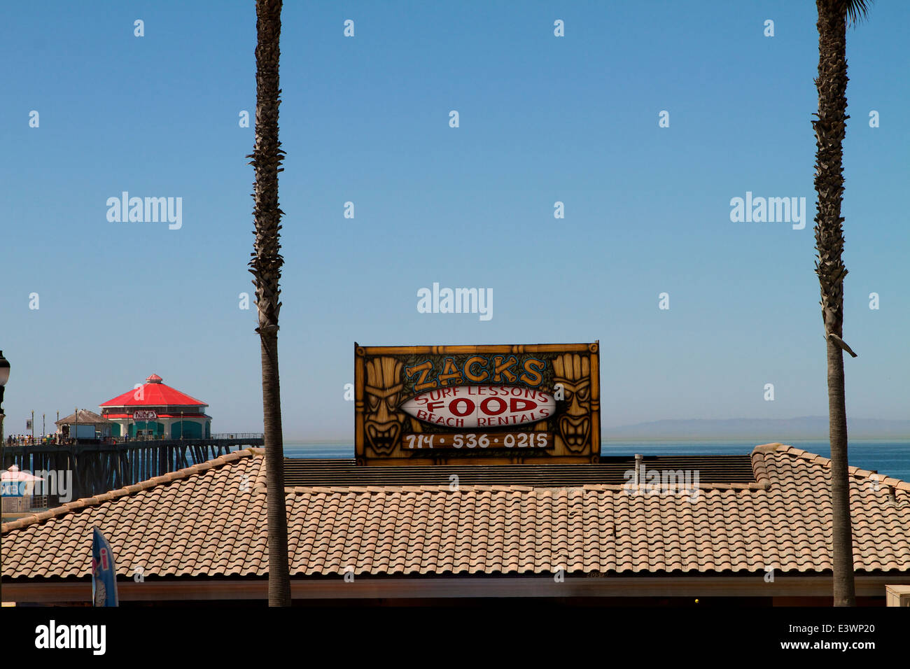 Sign on the store roof for zacks surf lessons and beach rentals with ruby's restaurant in the background at Huntington Beach ca Stock Photo
