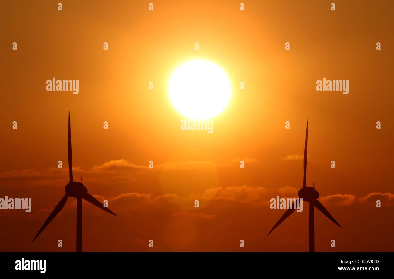 Two wind turbines are pictured in front of the sun near Ebersbach, Germany, 24 June 2014. Photo: Karl-Josef Hildenbrand/dpa Stock Photo