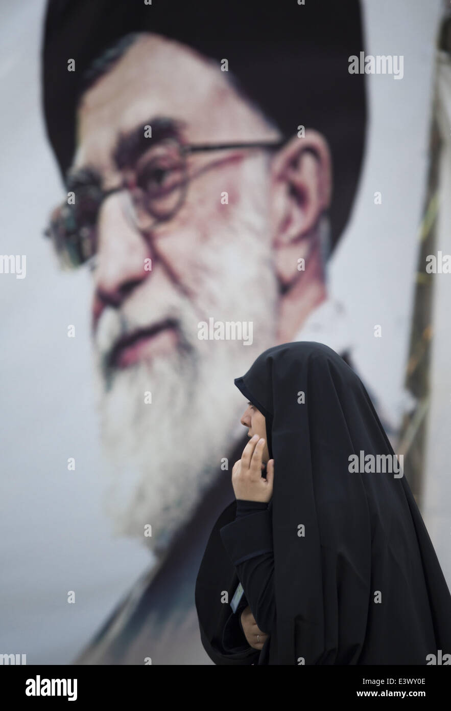 Tehran, Iran. 30th June, 2014. An Iranian woman walks past a portrait of Iran's Supreme Leader Ayatollah ALI KHAMENEI placed in the War museum while visiting of Tehran's Koran exhibition. The exhibition is an annual event during the month of Ramadan and this year, It is located in the War museum in the Iranian capital. Credit:  Morteza Nikoubazl/ZUMA Wire/ZUMAPRESS.com/Alamy Live News Stock Photo